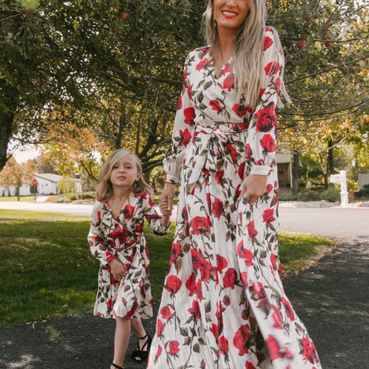 Mother and daughter in matching white dresses with red floral print, V-neck, long sleeves, and tie-waist.