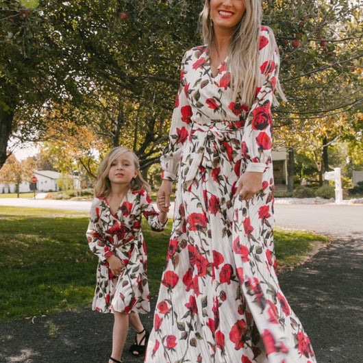 Mother and daughter in matching white dresses with red floral print, V-neck, long sleeves, and tie-waist.