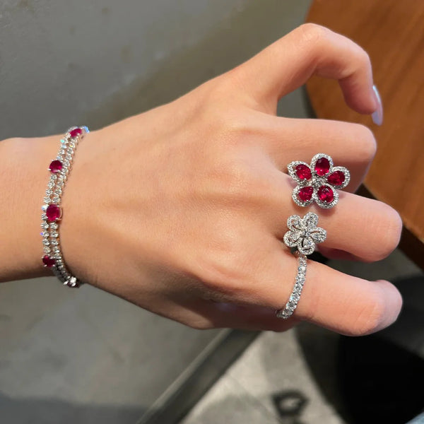 Silver-tone ring with two flower designs, one with crimson gemstones and clear zircons, the other with clear zircons.