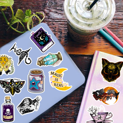 A hand holds a gothic-themed sticker featuring a raven, skull, and crystals, with a pile of 50 assorted waterproof stickers in the background.