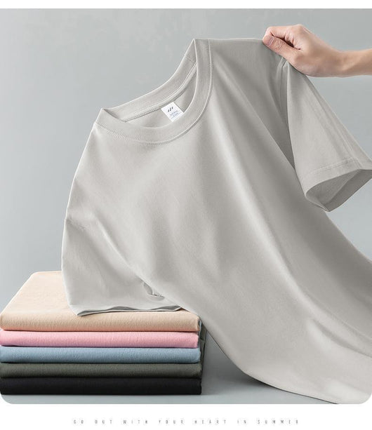 Light gray short-sleeve t-shirt with a round neck, held up to show its smooth fabric. A stack of folded t-shirts in various colors is visible in the background. - Image 24