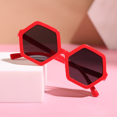 Red hexagonal children's sunglasses with dark lenses on a pink surface with a white block. - Image 12