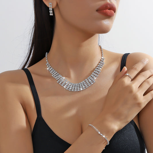 Sparkling four-piece jewelry set with a rhinestone necklace, bracelet, drop earrings, and a simple band ring on a model.