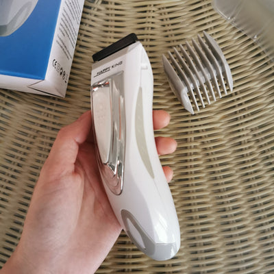 White and silver electric hair clipper held in hand, with a grey guide comb and blue packaging on a woven surface. - Image 13