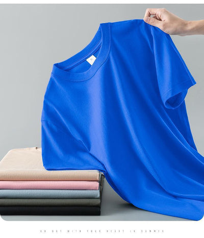 Light gray short-sleeve t-shirt with a round neck, held up to show its smooth fabric. A stack of folded t-shirts in various colors is visible in the background. - Image 23