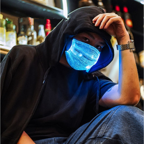 White LED mask with adjustable ear loops, a USB charging cable, and an instruction manual on a wooden surface.