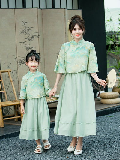 Mother and daughter in matching light green Chinese style cheongsam suits with patterned tops and solid skirts. - Image 6