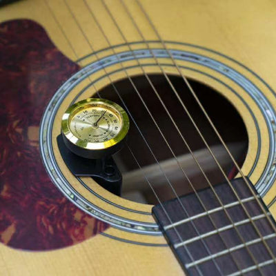 Black guitar humidifier with a gold hygrometer dial, shown with water splashes against a blue background and a guitar soundhole. - Image 3