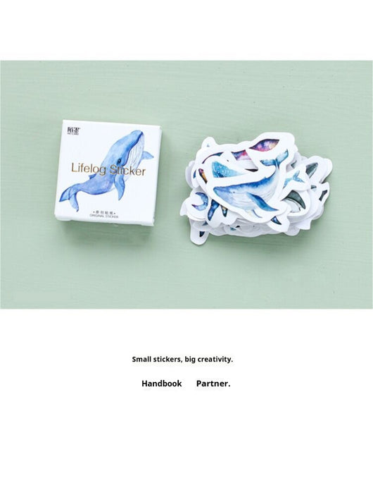 Box of 'Lifelog sticker' whale stickers with various blue whale designs scattered on a light blue plate. - Image 9