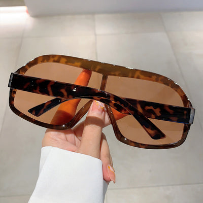 Oversized women's shield sunglasses with a tortoiseshell frame and brown-tinted lenses, held by a hand. - Image 10