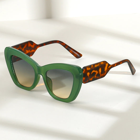 Pink cat-eye sunglasses with green temples and brown to pink gradient lenses on a white background.