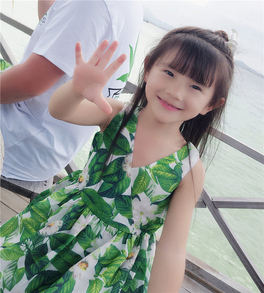 Boy in white t-shirt and floral shorts holding hands with girl in matching floral dress on a sunny beach. - Image 4