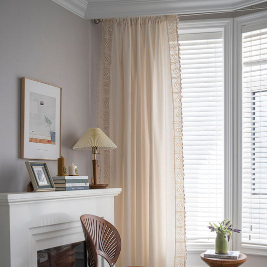 Close-up of a beige semi-transparent curtain with a delicate crochet lace trim and decorative tassels. - Image 2