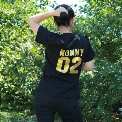 Child's black short-sleeved t-shirt with 'BABY 04' in gold print on the back, worn by a toddler in grass. - Image 8