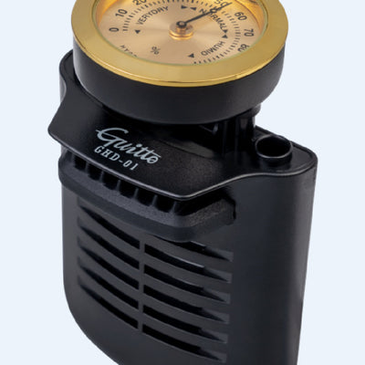 Black guitar humidifier with a gold hygrometer dial, shown with water splashes against a blue background and a guitar soundhole. - Image 5