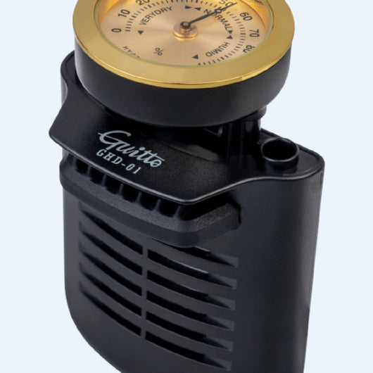 Black guitar humidifier with a gold hygrometer dial, shown with water splashes against a blue background and a guitar soundhole. - Image 5