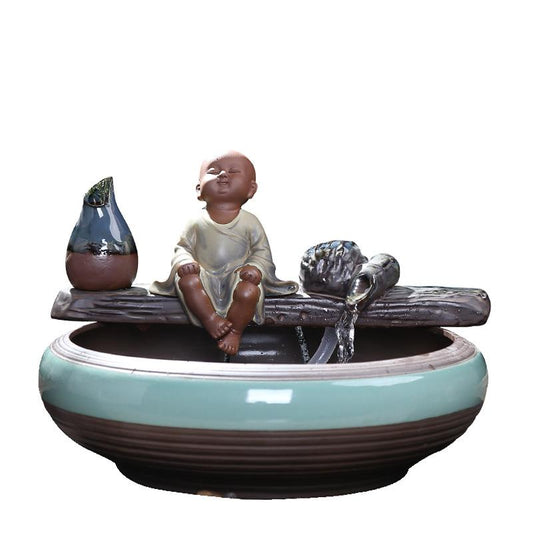 Ceramic flowing water ornament with a meditating monk figurine, small plant, and misting humidifier in a teal and brown bowl. - Image 2
