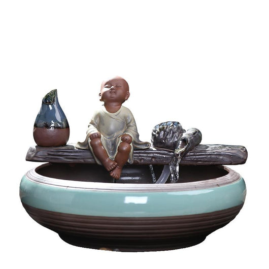 Ceramic flowing water ornament with a meditating monk figurine, small plant, and misting humidifier in a teal and brown bowl. - Image 2