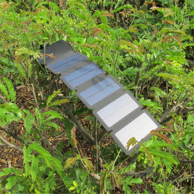 Black portable folding solar panel charger with six panels attached to a backpack in an outdoor setting. - Image 6