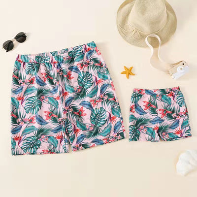 Family matching swimsuits with pink tropical floral and leaf print. Includes women's ruffled bikini, girl's one-piece, and men's/boy's swim shorts. - Image 8
