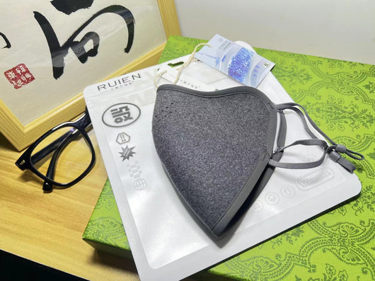 Dark gray cotton head-mounted mask with adjustable ear loops, shown in packaging on a patterned green surface. - Image 10