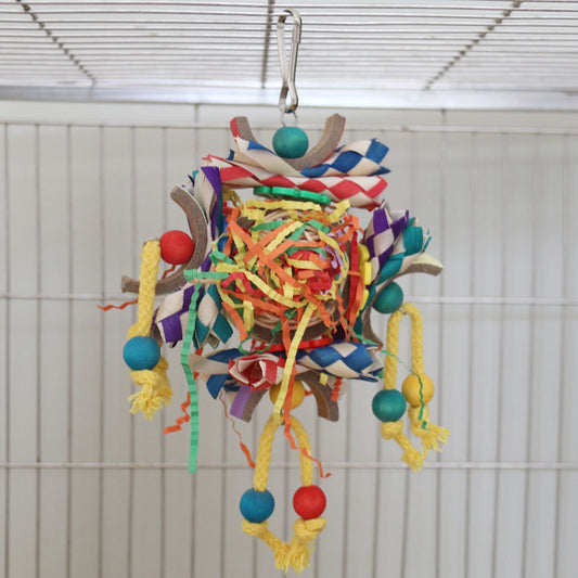 Colorful bird toy with paper tubes, shredded paper, and wooden beads, hanging inside a white wire bird cage.