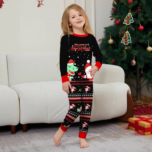Man wearing black Christmas pajamas with a cartoon dinosaur, Santa Claus, and "Merry Christmas" text, standing by a decorated tree. - Image 3