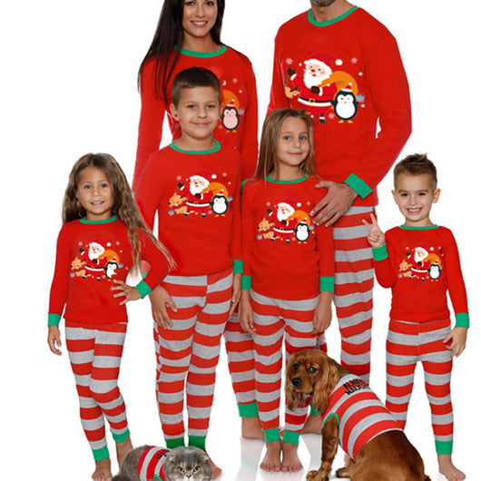 Family of five and pets wearing matching red and grey striped Christmas pajamas with Santa and penguin print.