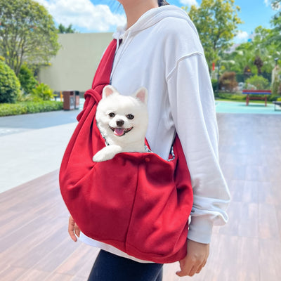 Person in white hoodie carrying a happy white dog in a navy blue pet sling bag outdoors. - Image 37