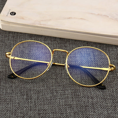 Gold round-frame anti-blue light glasses with clear resin lenses on a gray textured surface next to a notebook. - Image 9
