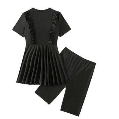 Woman in a black short-sleeve swim dress with ruffled details and matching swim shorts on a sandy beach. - Image 8