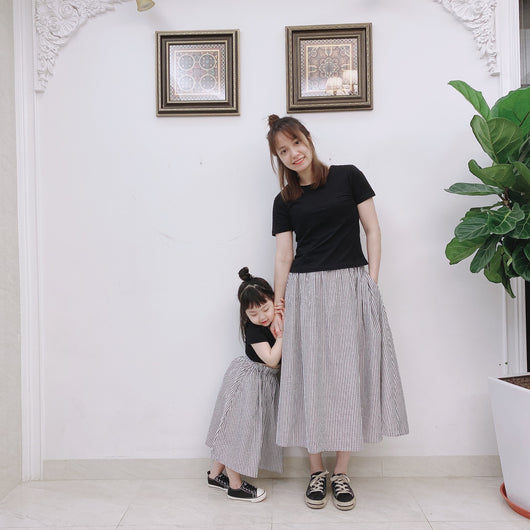 Young girl wearing a black short-sleeve crop top and a grey and white striped midi skirt with flip-flops. - Image 10
