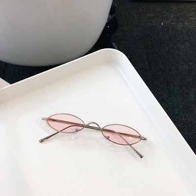 Silver-framed oval sunglasses with dark lenses reflecting a warm-toned object, displayed on a white tray. - Image 8