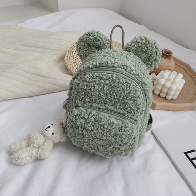 Pink fuzzy mini backpack with bear ears and a small white teddy bear keychain on a white bed. - Image 3