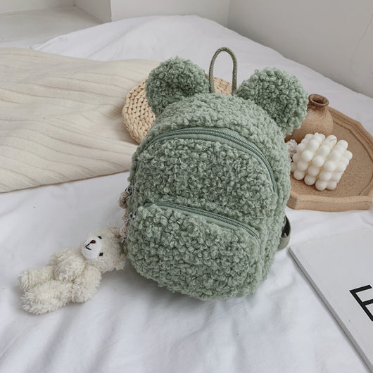 Pink fuzzy mini backpack with bear ears and a small white teddy bear keychain on a white bed. - Image 3