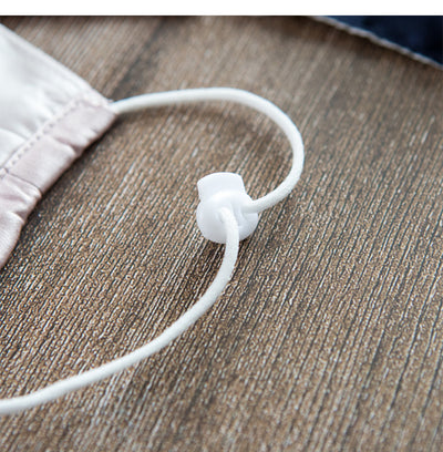 Light pink double layer silk face mask with adjustable white ear loops on an open magazine. - Image 8