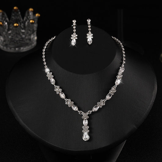 Elegant silver-tone necklace and matching drop earrings set with clear marquise and teardrop stones, displayed on a black bust.