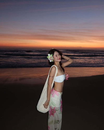 Woman in a white tube top with pink flower and a sheer floral maxi skirt, posing on a beach at sunset. - Image 10