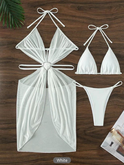White three-piece halter neck bikini and sheer cover-up set with a heart-shaped embellishment, laid flat on wood. - Image 11