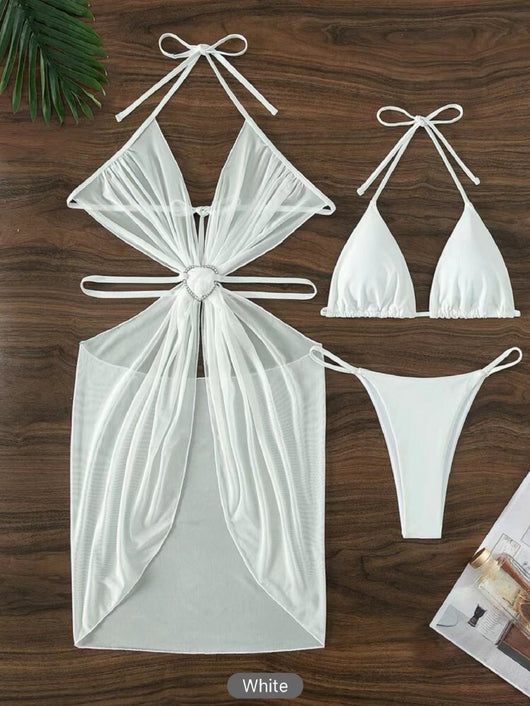 White three-piece halter neck bikini and sheer cover-up set with a heart-shaped embellishment, laid flat on wood. - Image 11