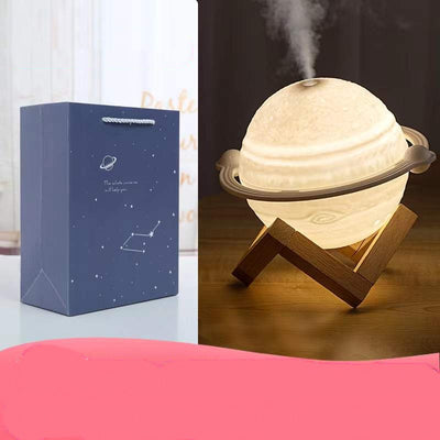 Yellow planet-shaped humidifier with a wooden stand emitting mist, next to a dark blue celestial gift bag. - Image 5