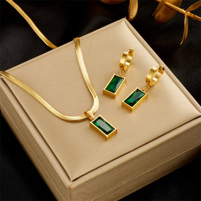 Gold hoop earrings with rectangular emerald green zircon pendants, displayed on a light beige fabric. - Image 8
