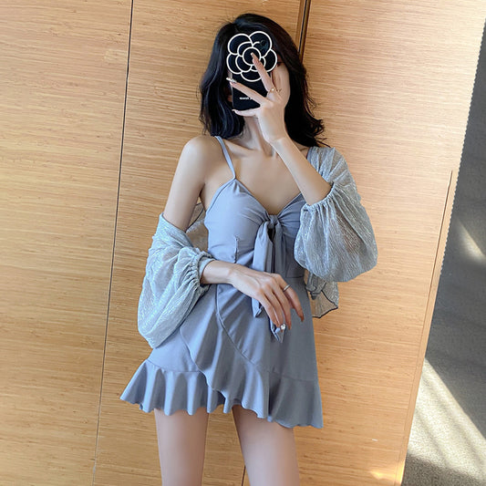 Women's light blue one-piece swimsuit with tie-front bust and ruffled hem, paired with a sheer shimmery cover-up.