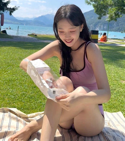 Women's light purple one-shoulder swimsuit with dark red contrast trim, lying on a striped blanket on green grass. - Image 10