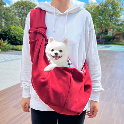 Person in white hoodie carrying a happy white dog in a navy blue pet sling bag outdoors. - Image 6