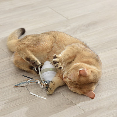 Golden-brown cat playing with a white and grey automatic rolling mouse cat toy with feather-like streamers on a wood floor. - Image 3