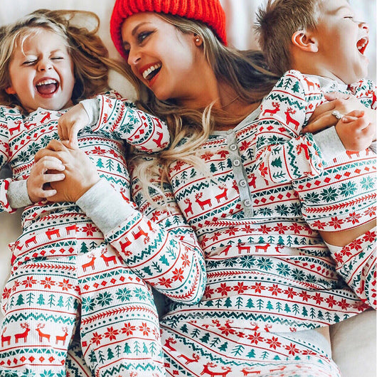 Family of four wearing matching white, red, and green fair isle Christmas pajamas with reindeer and snowflake patterns.