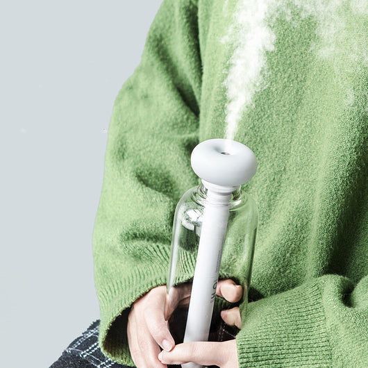 Clear bottle-shaped USB humidifier with a white donut-style top, emitting a stream of cool mist on a wooden table. - Image 5