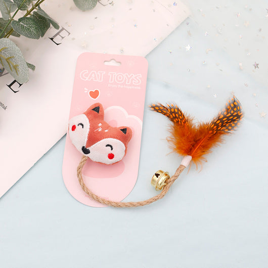 White cat head plush teaser toy with hemp rope, gold bell, and natural spotted feathers on pink packaging. - Image 9