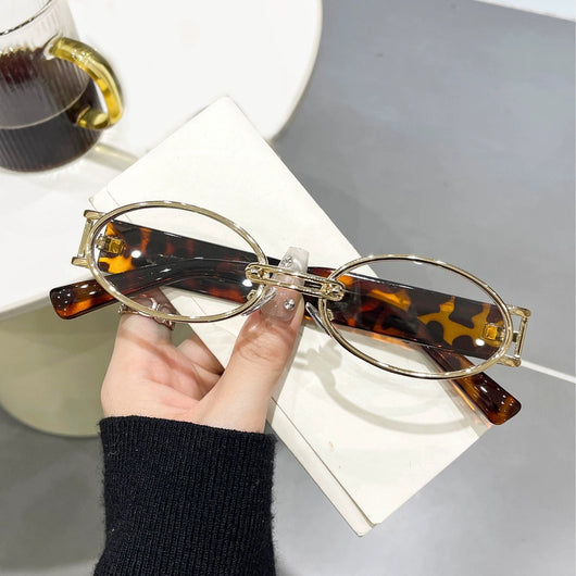 Retro small frame sunglasses with gold round frames and leopard print temples, held by a hand.